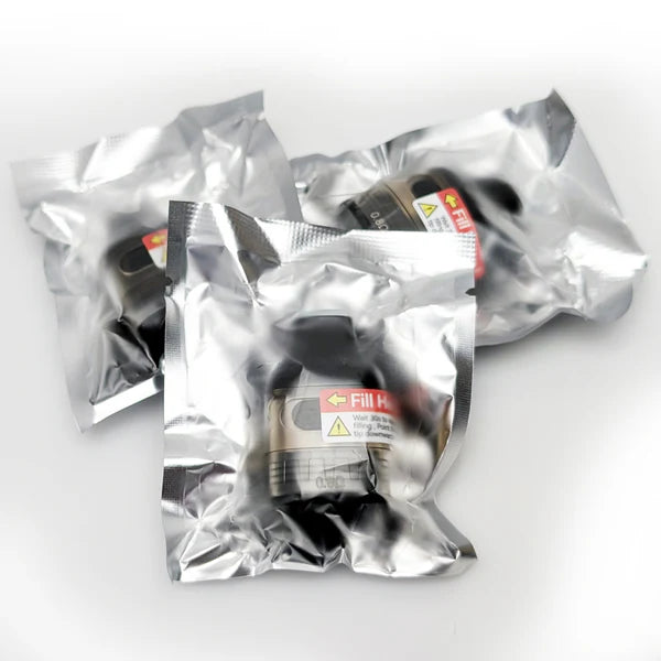 Three silver metallic foil pouches containing black cylindrical components with warning labels, arranged on a light gray background.